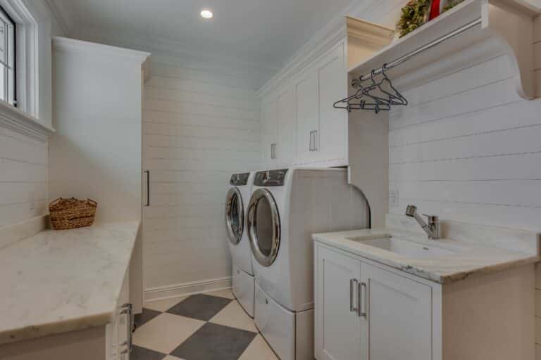 View of custom laundry room cabinets in South Bend, Indiana. White with cabinets, counter, sink, and walls